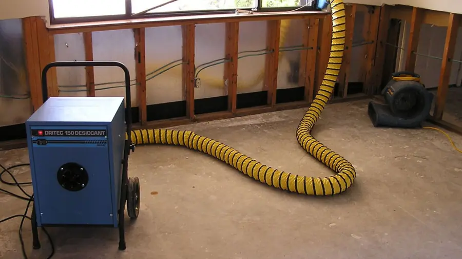 Dehumidifier with a yellow duct beside an opened wall